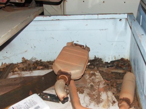 1965 Ford Mustang - An old exhaust muffler and pipes are visible among debris in the bed of a truck.