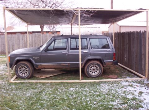 1987 Jeep Cherokee - A gray Jeep Cherokee is parked under a temporary shelter in a grassy yard with some snow on the ground.