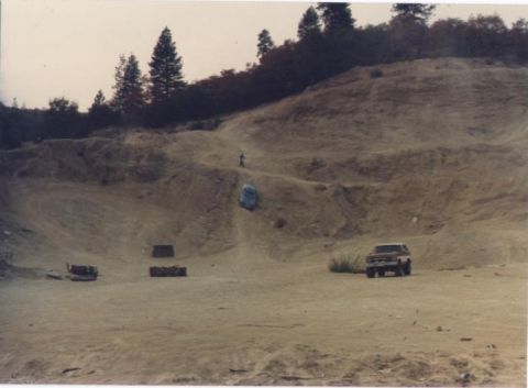 1990 Ford Bronco - A truck sits on a dirt road with a blue car on a hill in the distance.