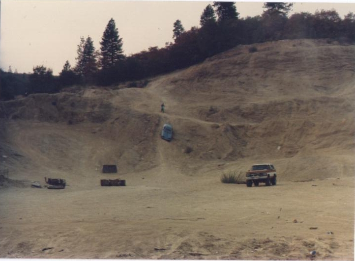 Truck and another vehicle on a dirt hill with trees in background