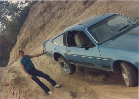 1990 Ford Bronco - A man poses with a blue coupe that is precariously positioned on a steep dirt slope.