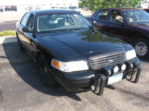 1999 Ford Crown Victoria - A black police car with a push bar and spotlights is parked on asphalt.