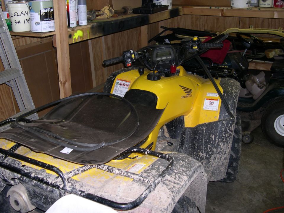 Mud-covered yellow Honda utility ATV parked in a wood-framed garage