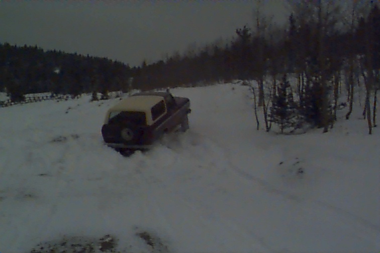 Red 1980 Ford Bronco with white top driving in snow, rear view