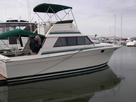 1982 Ford Bronco - A white cabin cruiser with green trim is docked in a marina, with other boats visible in the background.