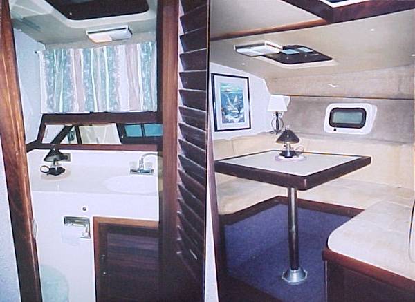 Boat interior with a galley and a dinette area, a sink, curtains, and a table with seating