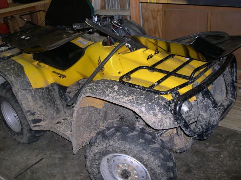 1982 Ford Bronco - Mud-covered yellow Honda ATV parked indoors.
