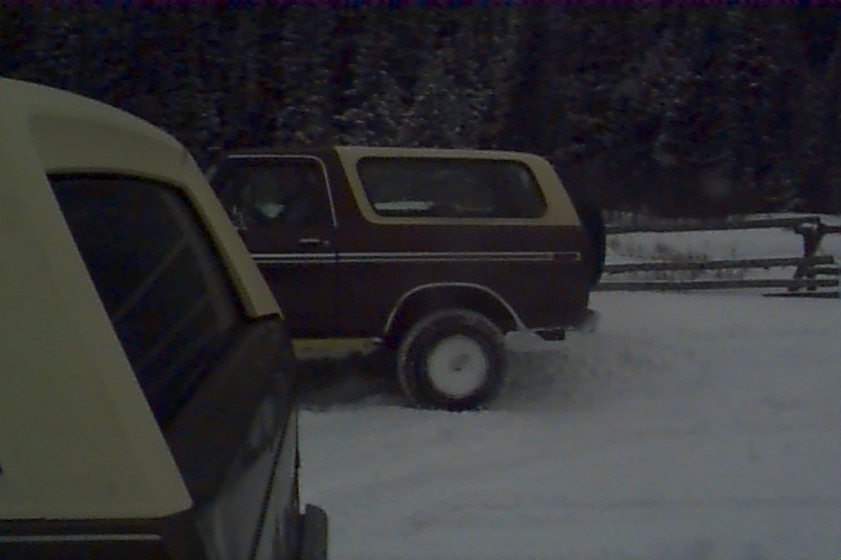 Brown and tan Ford Bronco parked in snow, another vehicle partially visible in foreground