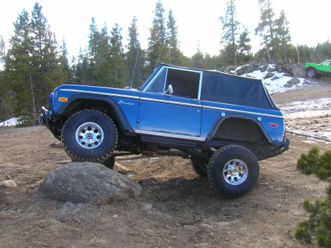 1979 Ford Bronco - This lifted blue Ford Bronco is navigating a rocky obstacle on an outdoor trail.