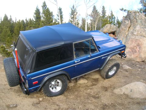 1979 Ford Bronco - This blue Ford Bronco is navigating a rocky, off-road trail with a soft top and spare tire visible.
