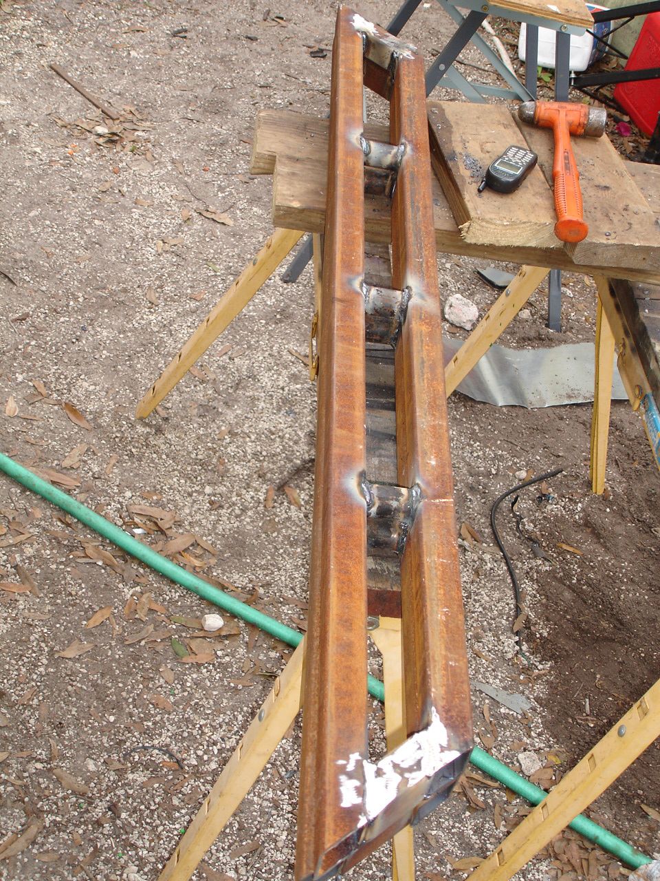 Welded steel sliders on sawhorses with a hammer and tape measure nearby