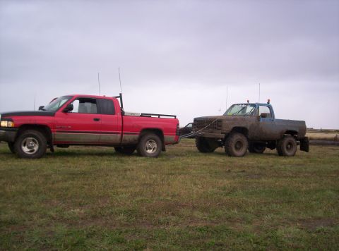 1989 Chevrolet Blazer - A red Dodge Ram tows a muddy blue Chevrolet K5 Blazer across a field under an overcast sky.