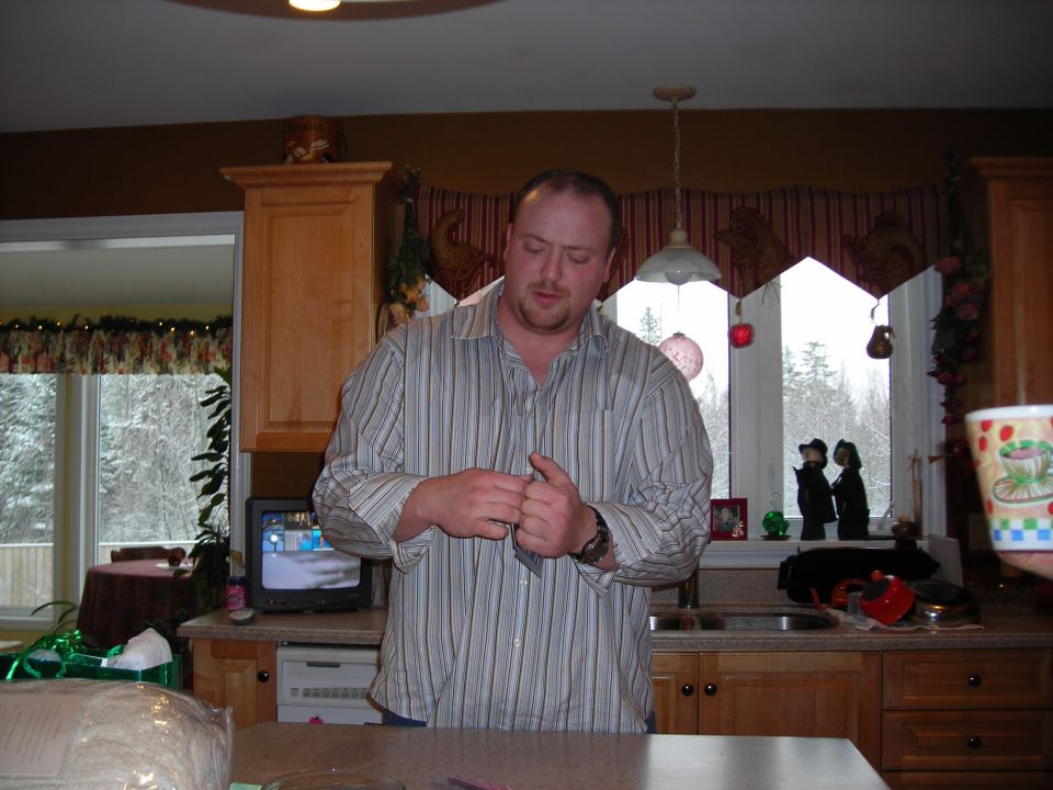 Man in a striped shirt stands in a kitchen, looking down at his hands