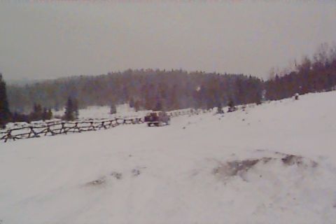 1980 Ford Bronco - A vehicle navigates a snow-covered terrain, with a rustic wooden fence bordering the path.