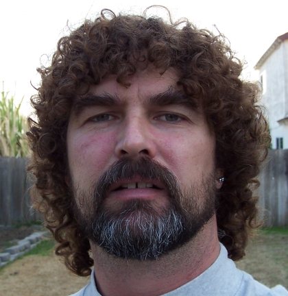 1990 Ford Bronco - A man with a full head of curly hair and a beard is shown from the chest up.