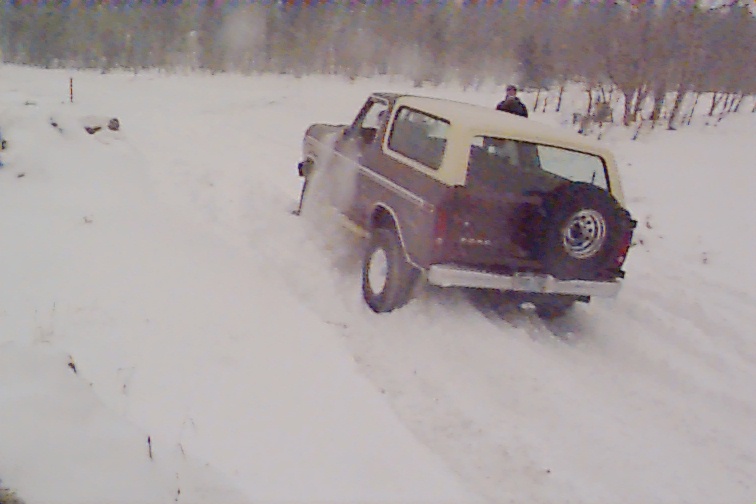 Brown and tan Ford Bronco with rear spare tire stuck in deep snow, viewed from rear quarter