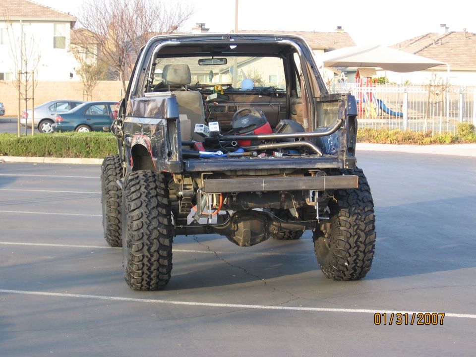 Rear of stripped, lifted dark Ford Bronco on large mud tires in a parking lot