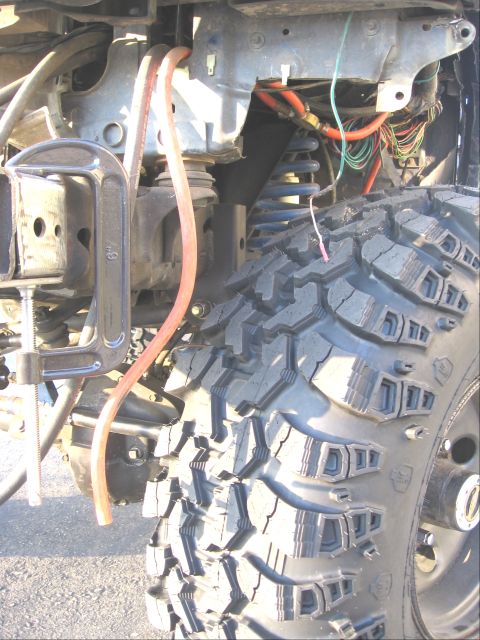 1994 Ford Bronco - The suspension and tire of a modified vehicle are shown, with a C-clamp attached to the frame for apparent work.