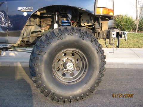1994 Ford Bronco - Close-up of a blue Ford Bronco's front wheel and fender, showing modifications and a "BRONCO" badge.