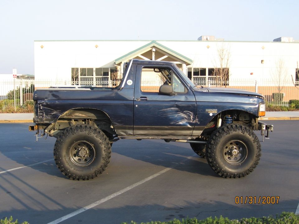 Dark blue lifted Ford Bronco on big mud tires, passenger side view in a parking lot