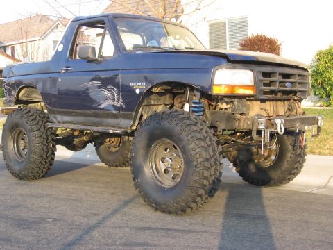 1994 Ford Bronco - This modified Ford Bronco features oversized tires and a lifted suspension, with visible damage on the side.