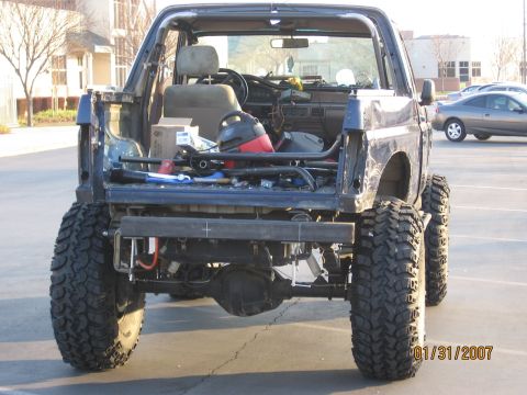 1994 Ford Bronco - This heavily modified SUV shows its rear end, oversized off-road tires and an exposed interior with a roll cage.