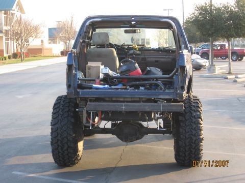 1994 Ford Bronco - Rear view of a modified blue SUV, showing its custom roll cage and large off-road tires.