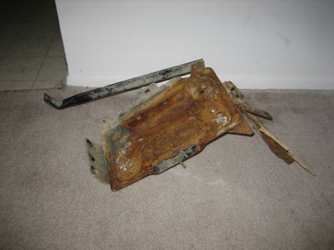 1990 Ford Bronco - This heavily rusted metal component appears to be a bracket or support from a vehicle's undercarriage.