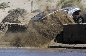 1999 Jeep Grand Cherokee - A silver SUV is stuck in the sand and water, with sand being thrown up by its wheels.