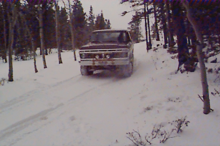 Brown 1978 Ford Bronco driving on a snowy road through a forest