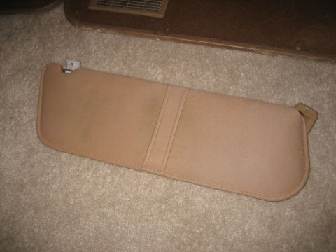 1990 Ford Bronco - A tan sun visor is shown lying on a carpeted surface, with a car vent visible in the background.