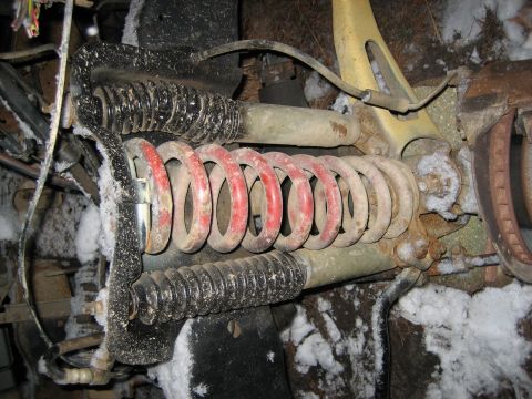 1990 Ford Bronco - Close-up of a vehicle's front suspension system, red and black coil springs partially covered in snow.