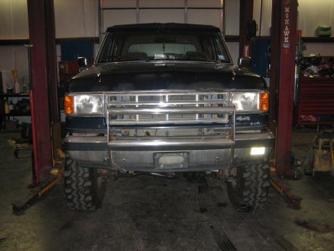 1990 Ford Bronco - This SUV is on a car lift in a garage, showing its front end with large tires and a prominent chrome grille.