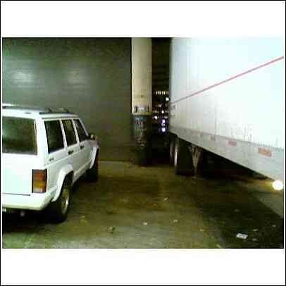 1994 Ford Bronco - A white Jeep Cherokee is parked next to a semi-trailer in what appears to be a loading dock or garage area.