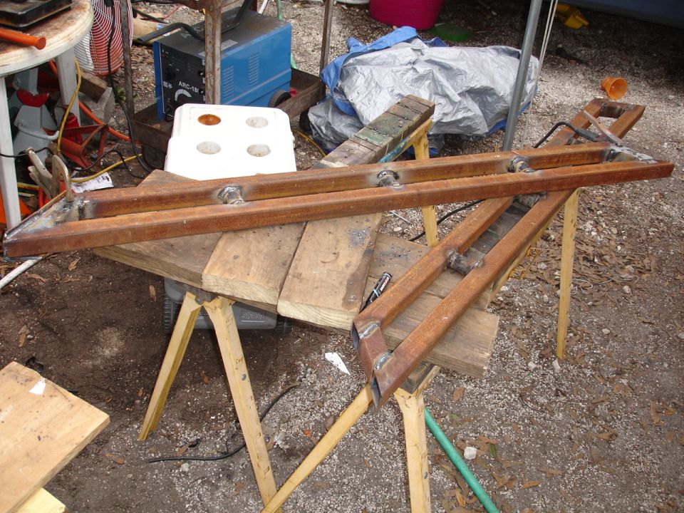 Two welded metal sliders on sawhorses, with a welder and other tools in the background