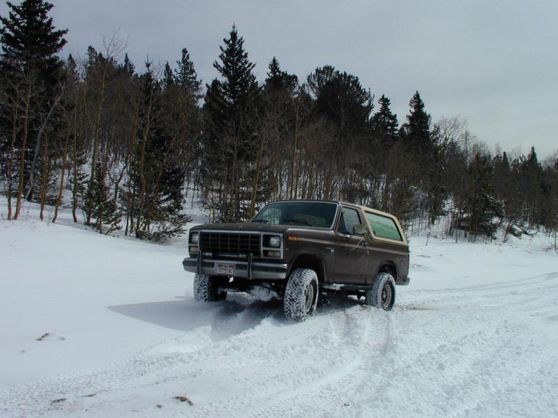 1980 Ford Bronco driving through snow with trees in background