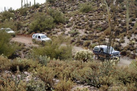 1991 Ford Bronco - Multiple vehicles navigate a dusty desert trail surrounded by arid vegetation and cacti.