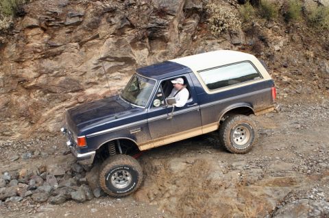 1991 Ford Bronco - A blue and tan Ford Bronco navigates a challenging rocky terrain, demonstrating its off-road capabilities.