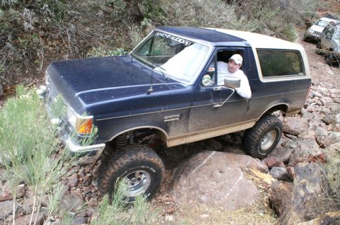 1991 Ford Bronco - A 1991 Ford Bronco tackles a challenging off-road trail with large rocks and vegetation.