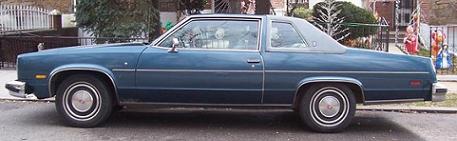 1999 Ford Crown Victoria - A blue two-door coupe is shown from the side, parked on a street with houses in the background.