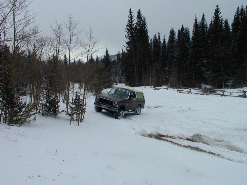 Brown 1980 Ford Bronco with a white top driving in snow, front-left quarter view