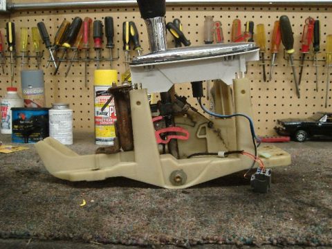 1992 Ford Crown Victoria - This automatic transmission shifter assembly features a chrome handle and beige plastic housing, shown on a workbench with tools in the bac…