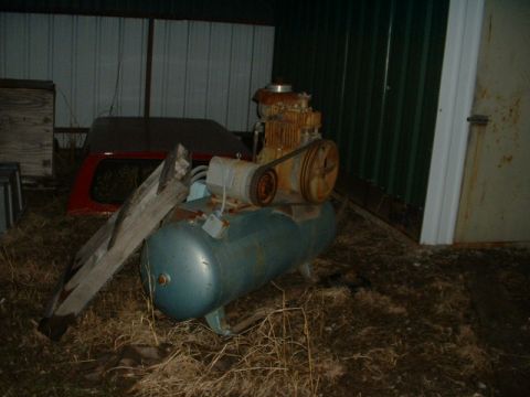 1965 Ford Mustang - An old air compressor unit with a blue tank and a rusty motor is stored outdoors.