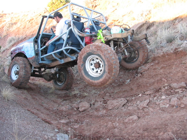 Off-road vehicle with roll cage on a dirt hill, driver visible, mud-splattered tires