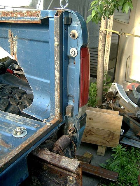 1988 Ford F-250 - Detail of a truck's rear corner, focusing on the tailgate hinge and taillight. Rust is present on the metal components.