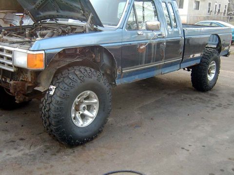 1988 Ford F-250 - A blue pickup truck with its hood up and modified suspension sits on a concrete surface.