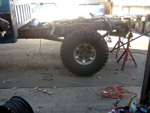 1988 Ford F-250 - The chassis of a truck is visible, supported by jack stands, with a large off-road tire prominently displayed.