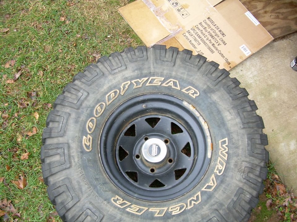 Close-up of a Goodyear Wrangler tire on a black rim, with a cardboard box in the background
