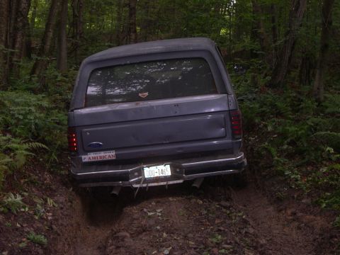 1989 Ford Bronco - Gray Ford Bronco navigates a muddy off-road trail in a wooded area.