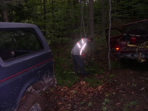 1989 Ford Bronco - A person uses a chainsaw in a wooded area next to a Ford Bronco and a pickup truck.